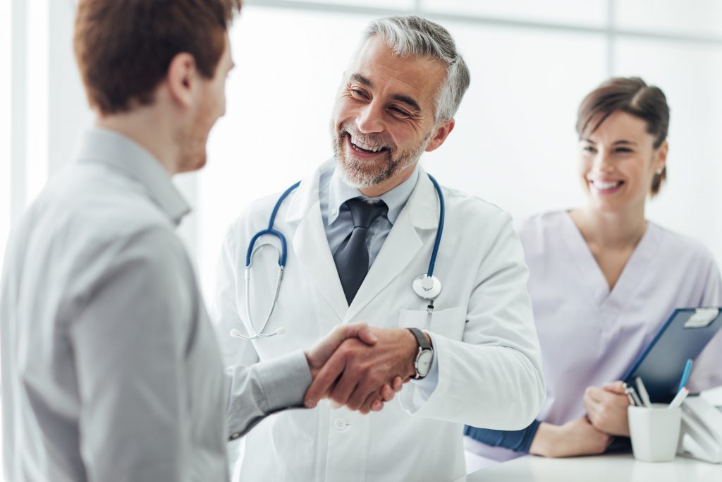 Médico sonriente estrechando la mano con paciente en consulta